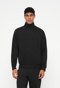 Μαύρο πουλόβερ από μαλακό ύφασμα, με ψηλό γιακά, μισό φερμουάρ και διακριτική λεπτομέρεια λογοτύπου στο στήθος, συμπληρωμένο από ribbed μανσέτες.