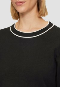 Zwarte gebreide trui met een ribbelige ronde halslijn en een contrasterende witte afwerking. Vloeibare textuur en aansluitend ontwerp zijn zichtbaar.