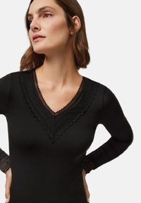 Top negro de manga larga con un detalle de encaje en forma de V en capas y acentos de encaje en las mangas, hecho de una tela suave y elástica.