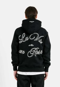Felpa nera con grande scritta bianca ricamata "La Vie en Rose." Presenta una vestibilità comoda, maniche lunghe e una classica tasca a marsupio.