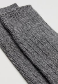 Grå, ribbade strumpor gjorda av texturerat tyg. Har en platt mudd och ett vertikalt ribbmönster som visar en mjuk, stickad yta.