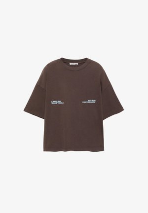 Ohlapna rjava majica s kratkimi rokavi in okrolim izrezom, na sredini ima napis "Občutek, ki postane viden" in "Ne za nastope" v svetlo modri pisavi.