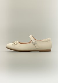 Μπεζ μπαλαρίνα με στρογγυλερή μύτη, λεπτομέρεια φιόγκου στο μπροστινό μέρος και ρυθμιζόμενο λουράκι με ασημί αγκράφα. Λείο δερμάτινο υλικό.