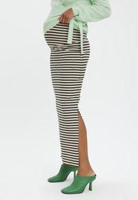 Stribet sort og hvid nederdel med sideslid, parret med grønne hælede mules og en lysegrøn sweater. Glat stof med tætsiddende design.