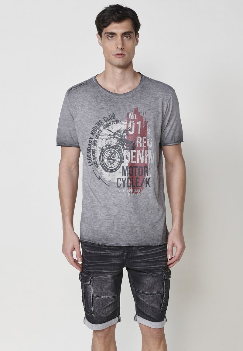 Camiseta gris de cuello redondo con un diseño desvanecido y un gráfico de motocicleta. Combinada con pantalones cortos negros con bolsillos de carga y dobladillos enrollados.