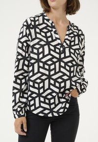 Zwart-wit blouse met lange mouwen en een geometrisch kubuspatroon, voorzien van een V-hals en een relaxte pasvorm, gemaakt van lichte stof.