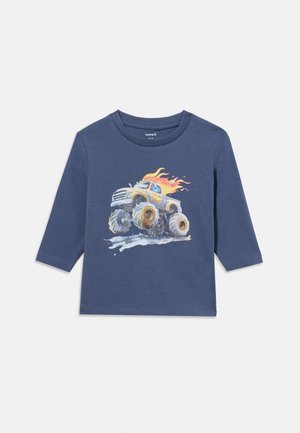 Chemise enfant à manches longues bleu marine avec un dessin d'un monster truck avec des flammes sur le dessus roulant sur de la boue.
