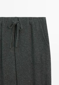 Donkergrijze gebreide sweatpants met een elastische tailleband en een strikkoord, inclusief zijzakken, tentoongesteld tegen een witte achtergrond.