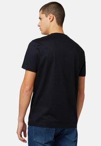 Juodas medvilninis marškinėliai su klasikinėmis apvalios formos iškirptėmis ir trumpomis rankovėmis, pasižymintys lygia tekstūra. Atgaliniame vaizde paprastas dizainas, be grafikos.