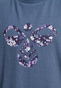 Blauwe katoenen T-shirt met een bloemmotief in paarse en witte tinten, gevormd als een gestileerde vlinder of abstract ontwerp.
