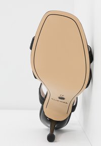 Chaussure noire à talon haut vue par la semelle, montrant une semelle beige taille 37 et un talon fin sur fond blanc.