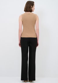 Braun geripptes, ärmelloses Top kombiniert mit hoch taillierten schwarzen Hosen, die eine figurbetonte Silhouette und einen eleganten Stoffbesatz aufweisen.