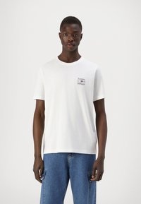Biała bawełniana koszulka z małym nadrukowanym logo w kolorze granatowym z tekstem "Tommy Hilfiger". Klasyczny okrągły dekolt i krótkie rękawy.