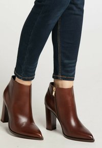 Braune Leder-Stiefeletten mit spitzem Zehenbereich und hohem Blockabsatz, ausgestattet mit einem seitlichen Reißverschluss und glatter Textur.