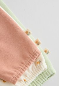 Shorts di cotone nei colori pesca, crema e verde menta, con motivi floreali e bande elastiche in vita. Orli arrotondati con piccole etichette.