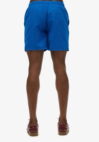 Pantaloni da bagno blu royal con vita elastica e tasche laterali, caratterizzati da una texture liscia e un orlo dritto.