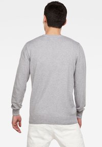 Hellgrauer Pullover mit langen Ärmeln, rundem Ausschnitt und weicher Textur. Zeigt ein sauberes, schlichtes Design ohne sichtbare Muster oder Akzente.