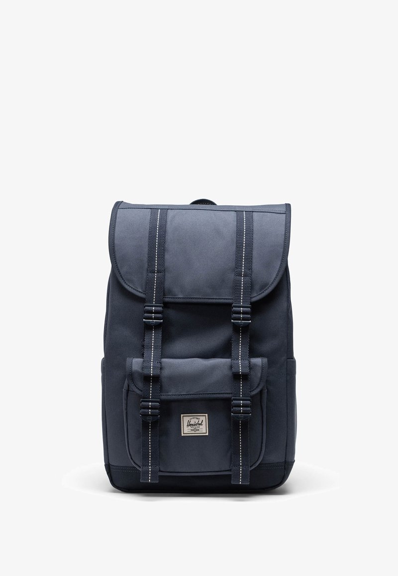Navy plavi tkani ruksak s preklopnim vrhom, dva prednja remena, prednjim džepom i bijelim šavom. Herschel brend oznaka na prednjoj strani.