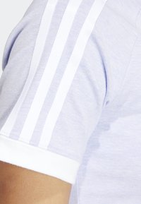 Light purple short-sleeve shirt with white ribbed cuffs and three white stripes along the shoulder. Soft, textured fabric.