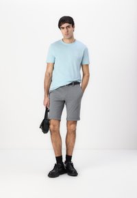 Lyseblå T-skjorte med rund hals, grå rullede shorts, svart belte, svarte sko, og en liten svart skulderveske. Glatt tekstur, uformell design.