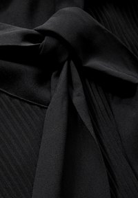 Tissu noir au toucher doux, avec un détail de nœud noué et des éléments de conception plissés sur les bords. Apparence élégante et structurée.