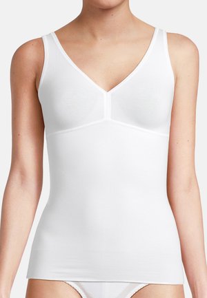 Frau trägt ein eng anliegendes weißes ärmelloses Top mit V-Ausschnitt und passende weiße Unterwäsche vor einem einfarbigen Hintergrund.