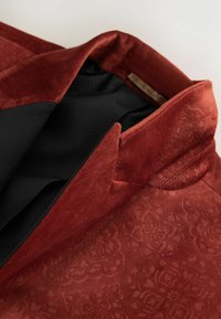 Rotvelvet-Blazer mit einem strukturierten Blumenmuster, ausgestattet mit einem schwarzen Stofffutter und einem Reverskragen.