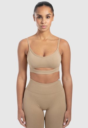 Beige sportbeha met dunne bandjes, een uitsnijding aan de voorkant en een gladde textuur. Gecombineerd met bijpassende high-waisted leggings.