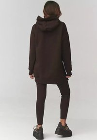 Czarna bluza z dużym kapturem i długimi rękawami, zestawiona z czarnymi prążkowanymi legginsami i masywnymi czarnymi sneakersami. Prosty, schludny design.