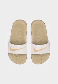 Ζευγάρι μπεζ σαγιονάρες Nike με υφασμάτινες σόλες και λευκά λουράκια που φέρουν πορτοκαλί λογότυπα Nike swoosh.