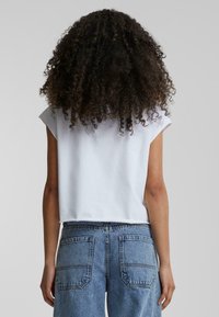 Fehér, rövid ujjú, cropped póló, amelyet magas derékú kék farmernadrággal párosítottak, amelyen két hátsó zseb és kopottas textúra található.