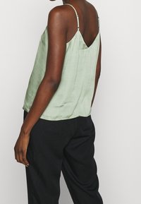 Ljusgrön sidenkamisol med justerbara spaghettiaxlar och ett V-format bakstycke, med en avslappnad passform och mjuk textur.