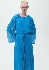 Rochie din chiffon albastru, cu mâneci lungi și fluide, decolteu rotund și talie legată. Materialul are o textură moale, transparentă, cu pliseuri.