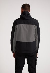 Giacca da uomo in nero e grigio. Presenta un cappuccio, design a blocchi di colore e un tessuto leggero e liscio. Include polsini elasticizzati e una vestibilità comoda.
