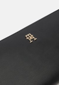 Portofel din piele neagră cu finisaj texturat, având un logo auriu proeminent și cusături îngrijite de-a lungul marginii.