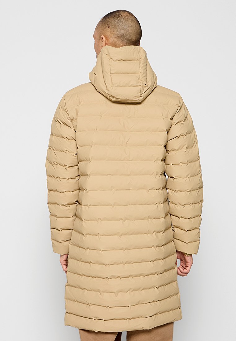 Manteau doudoune beige avec capuche. Design matelassé vertical, longueur mi-genoux. Texture lisse, poignets élastiques et fermeture éclair avant dissimulée.