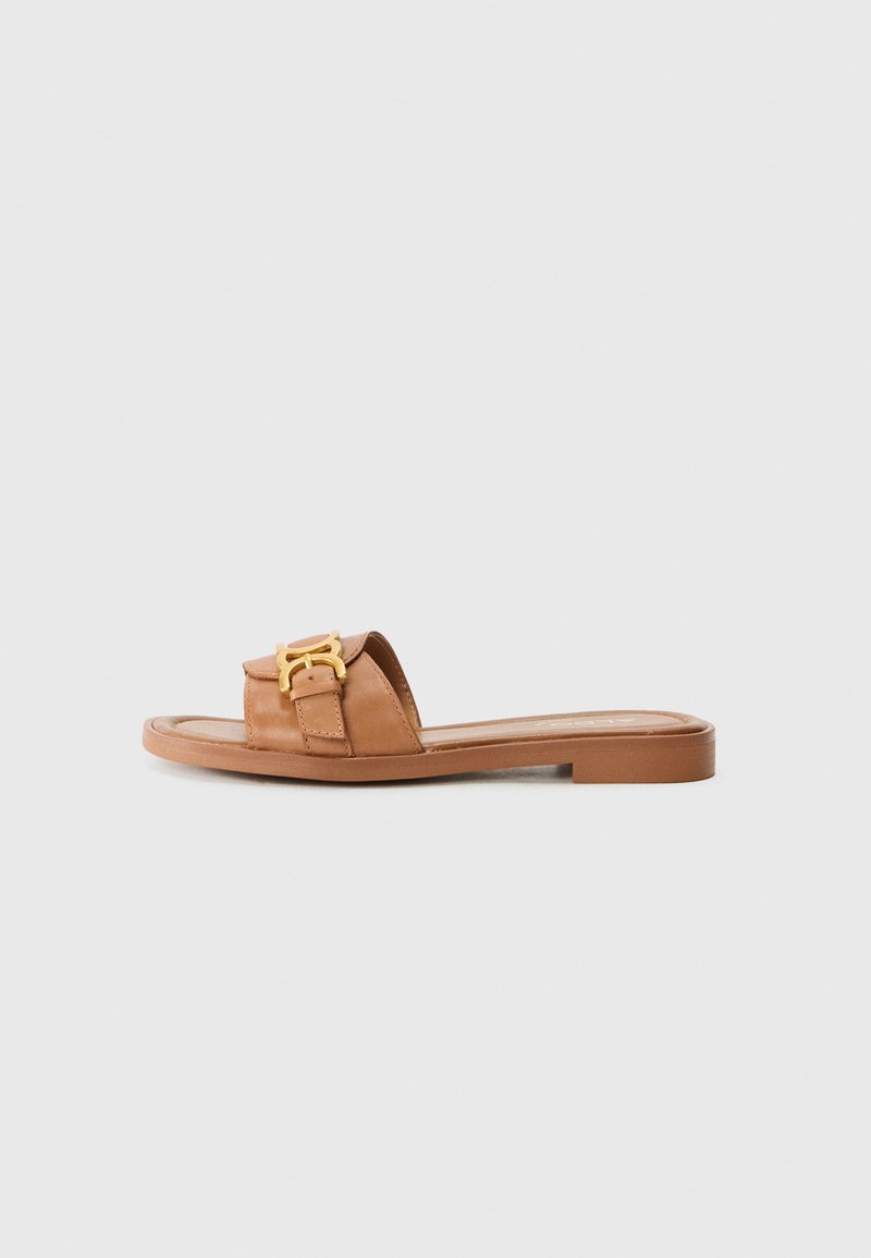 Sandale en cuir marron avec une large lanière, accents en métal doré, semelle plate et design minimaliste. Convient pour une tenue décontractée.