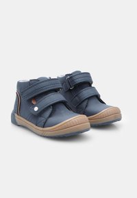 Tumes sinine laste kingade paar, millel on kaks Velcro rihma ja heledast pruunist kummitaldad valgel taustal.