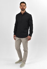 Zwarte overhemden met lange mouwen, beige broeken en lichtgrijze instappers. Glad stof, slim fit, minimalistisch ontwerp.