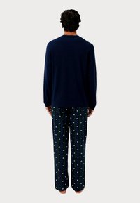 Námořnický dlouhý rukáv s kulatým výstřihem, spárovaný se zelenými kostkovanými kalhotami s bílými vzory. Měkká tkanina, volný střih a rovné nohavice.