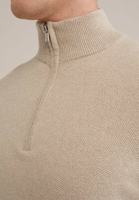 Beige kötött félcipzáras pulóver ribbelt gallérral és sima textúrával. Ezüst cipzárral és finom szövött mintával rendelkezik.
