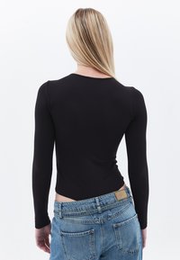 Schwarzer Langarm-Body mit rundem Ausschnitt, kombiniert mit hellblauen, hochgeschnittenen Jeans aus Denim, die ein sichtbares Patch am Bund aufweisen.