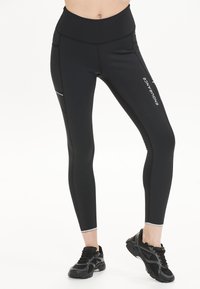 Zwarte high-waisted leggings gemaakt van rekbaar materiaal, met zijzakken, reflecterende accenten en een gladde textuur.