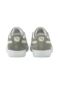 Sapatilhas de camurça cinza com solas de borracha brancas, colarinhos acolchoados e detalhes em ouro no calcanhar e na língua, apresentando uma superfície texturizada.