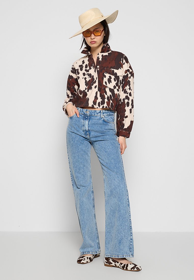 Krótka bluzka w zwierzęcy wzór w brązowo-kremowych odcieniach, w połączeniu z jasnoniebieskimi dżinsami dzwonami oraz balerinami w zwierzęcy wzór. Całość dopełnia słomkowy kapelusz.