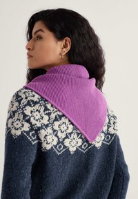 Pletený sveter s tmavomodrým telom a bielymi kvetinovými vzormi, s purpurovým skladaným rebrovaným golierom. Viditeľné náušnice v tvare ucha.