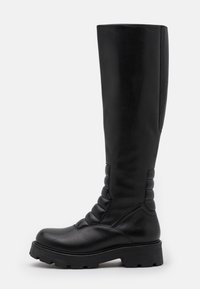Botas altas de cuero negro hasta la rodilla con puntera redondeada, paneles laterales texturizados y suela de goma gruesa. Presenta detalles de costura en la parte frontal.
