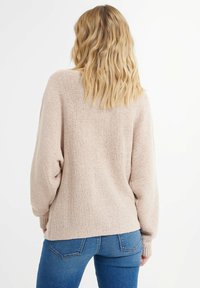 Light pink, textured knit sweater with loose fit and dropped shoulders. Features ribbed cuffs and hem, paired with blue fitted jeans.