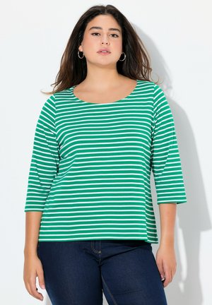 Top a righe verdi e bianche con scollatura a barca e maniche a tre quarti, realizzato in un tessuto morbido. Indossato con jeans blu scuro.