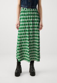 Jupe maxi verte à motifs avec un design géométrique présentant des nuances alternées de vert et de noir ; taille élastique, tissu fluide.